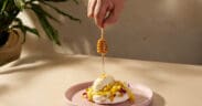Honey being drizzled over the Abejas Pavlova dessert with mango, whipped cream and coconut ice cream.