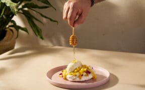Honey being drizzled over the Abejas Pavlova dessert with mango, whipped cream and coconut ice cream.