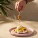 Honey being drizzled over the Abejas Pavlova dessert with mango, whipped cream and coconut ice cream.