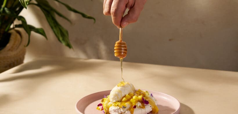 Honey being drizzled over the Abejas Pavlova dessert with mango, whipped cream and coconut ice cream.