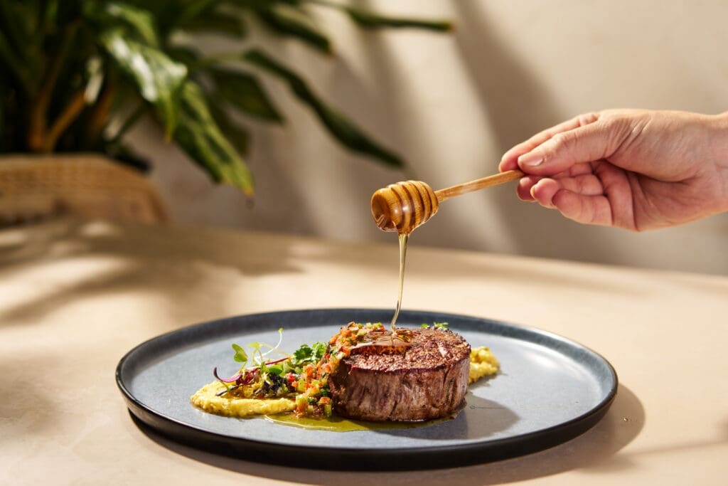 Beef tenderloin entrée with roasted corn ragout and vegetables drizzled with honey.