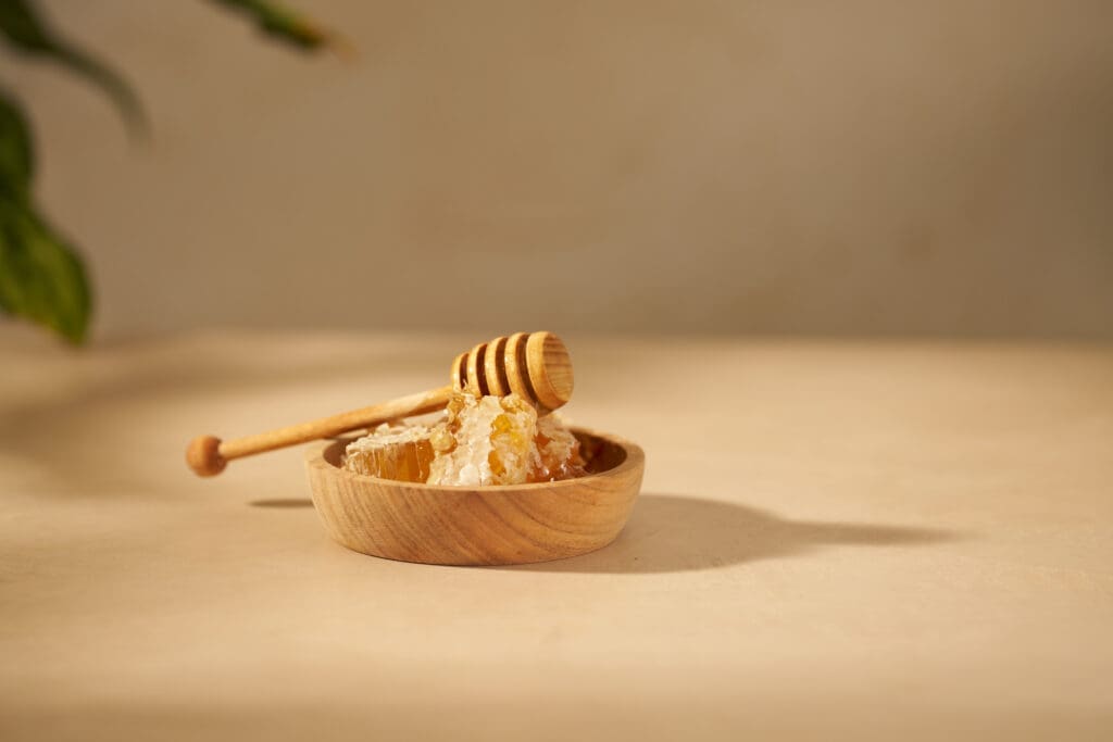 Honeycomb and honey dipper in a wooden bowl representing pollinator ingredients used in the Viva Abejas menu.