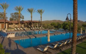 Resort-style pool complex at Rancho de los Caballeros in Wickenburg, Arizona with palm trees, lounge chairs and desert mountains in the background.