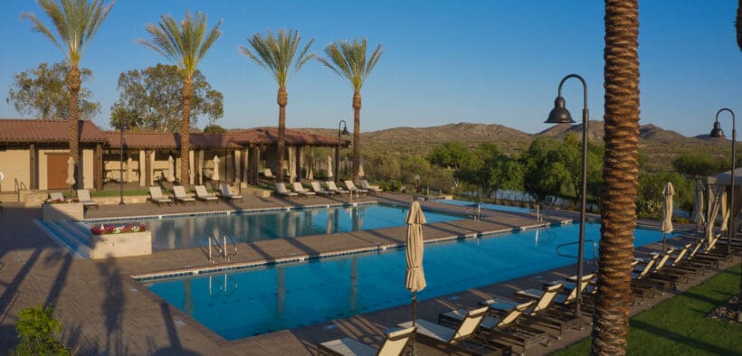 Resort-style pool complex at Rancho de los Caballeros in Wickenburg, Arizona with palm trees, lounge chairs and desert mountains in the background.