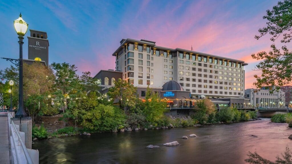 Exterior of Renaissance Reno Downtown Hotel & Spa at sunset overlooking the Truckee River with colorful sky reflections and city lights.