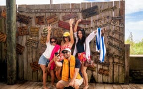 Group of friends posing for a photo in front of a rustic wooden sign display on South Padre Island.