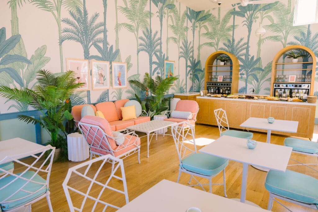 Interior of Pavilion Hotel Lanai dining space with palm wallpaper, pastel seating and breakfast setup in Avalon Catalina Island hotel.