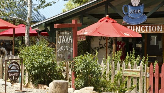 Colorful coffee shop patio with red umbrellas and rustic signage in Madrid, New Mexico.