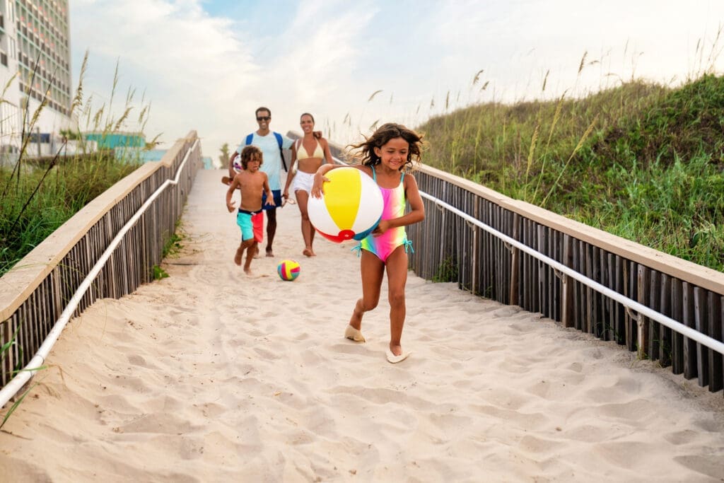 Family walking along a sandy beach path carrying a colorful beach ball on South Padre Island.
