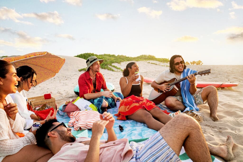 Group of friends relaxing on the beach with a guitar and drinks during a sunny day on South Padre Island.