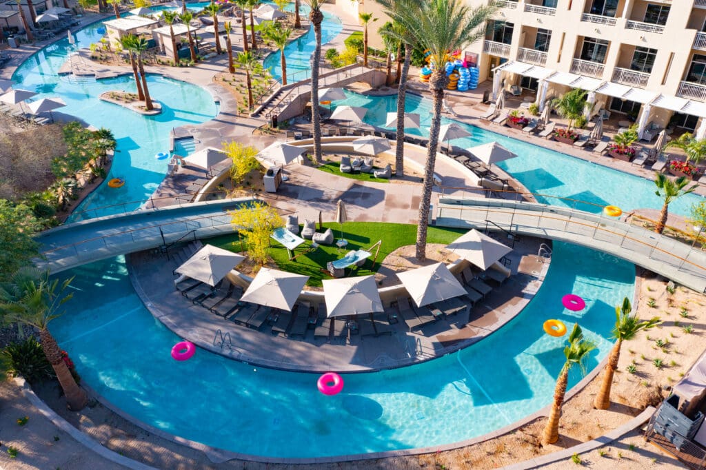 Aerial view of JW Marriott Phoenix Desert Ridge’s AquaRidge WaterPark featuring a winding lazy river, palm trees, cabanas and bright pool floats in Phoenix, Arizona.