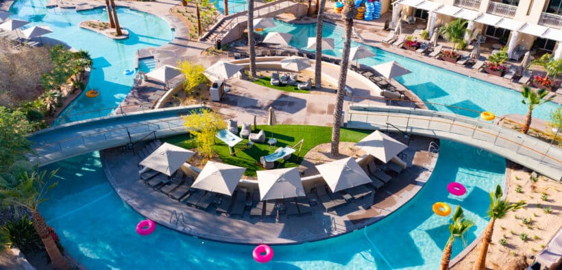 Aerial view of JW Marriott Phoenix Desert Ridge’s AquaRidge WaterPark featuring a winding lazy river, palm trees, cabanas and bright pool floats in Phoenix, Arizona.