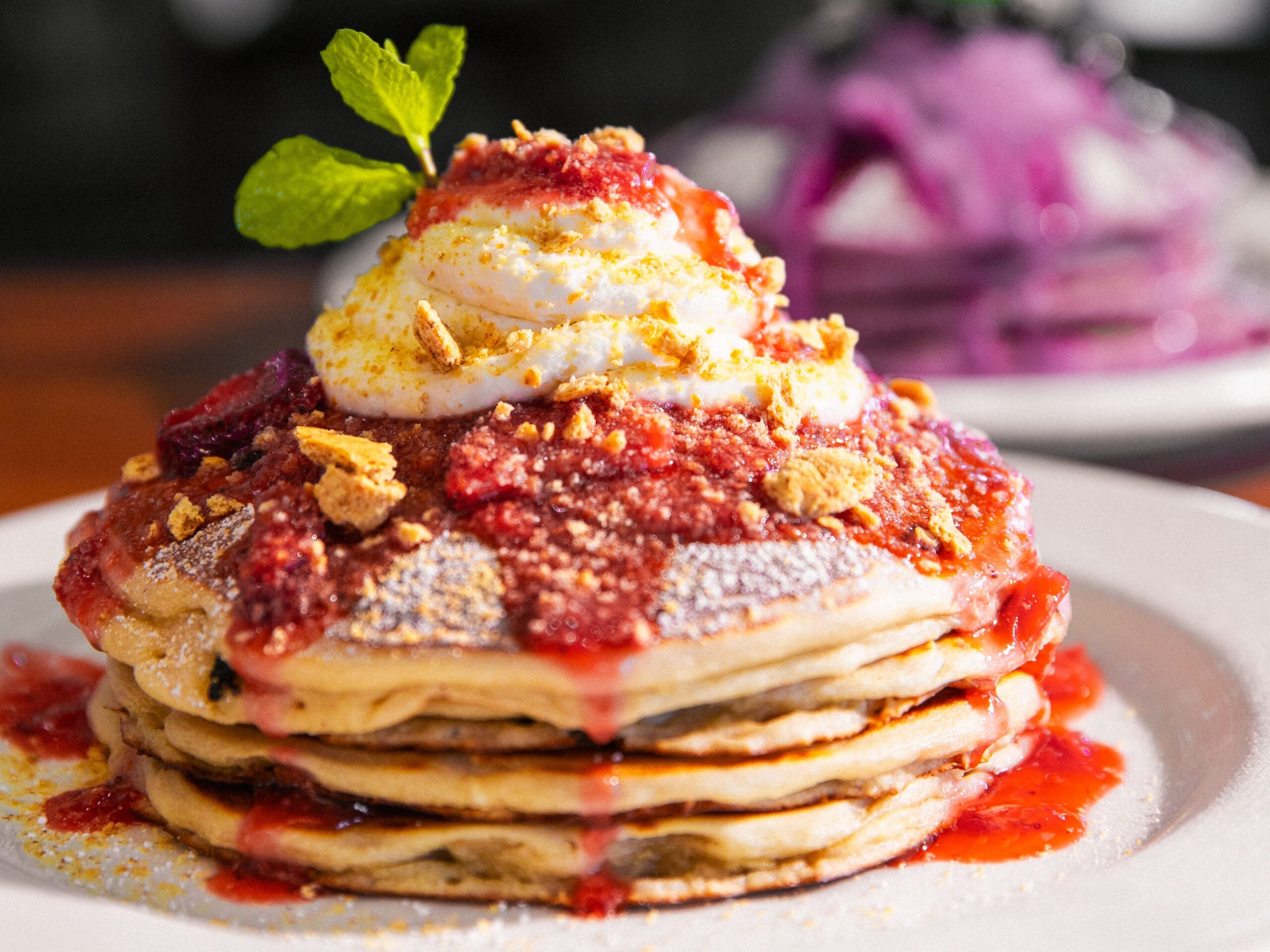 Stack of strawberry shortcake pancakes topped with whipped cream, fruit and crumble at Hash Kitchen.