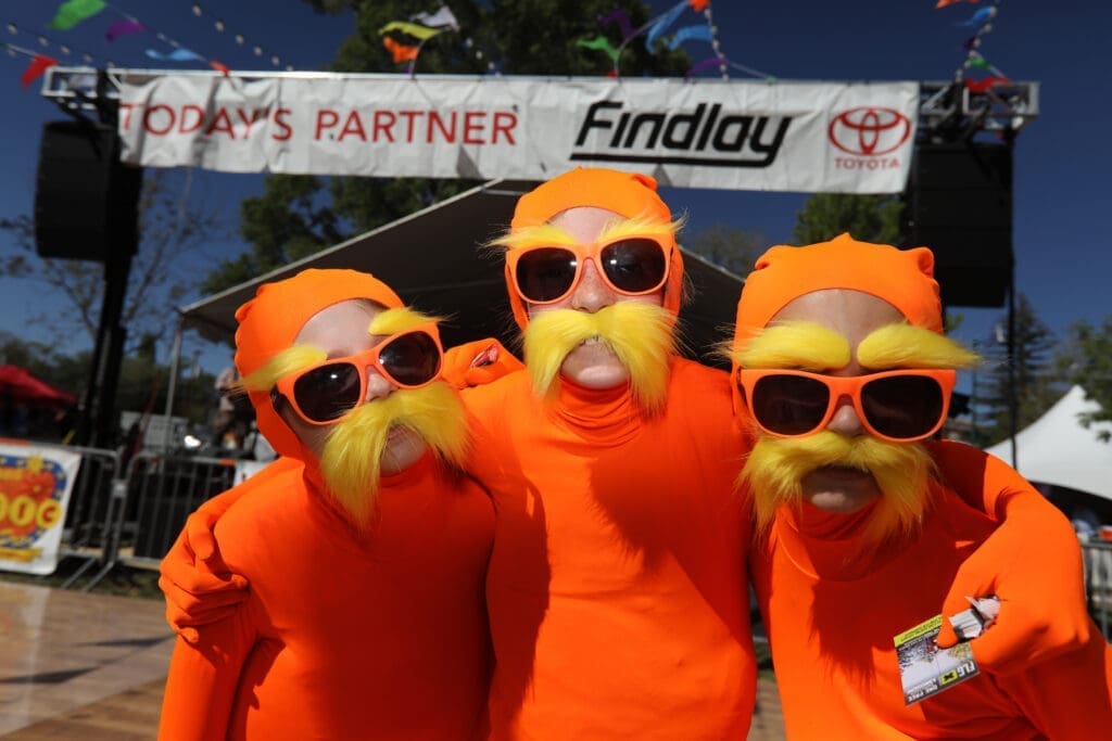 Three people dressed in bright orange Lorax costumes with sunglasses and fake mustaches posing at the Flagstaff Hullabaloo Festival.