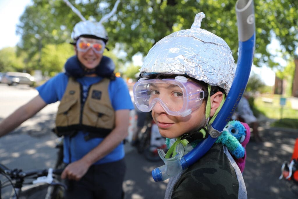 Woman and child smiling at a festival while wearing animal-themed hats, surrounded by colorful decorations.