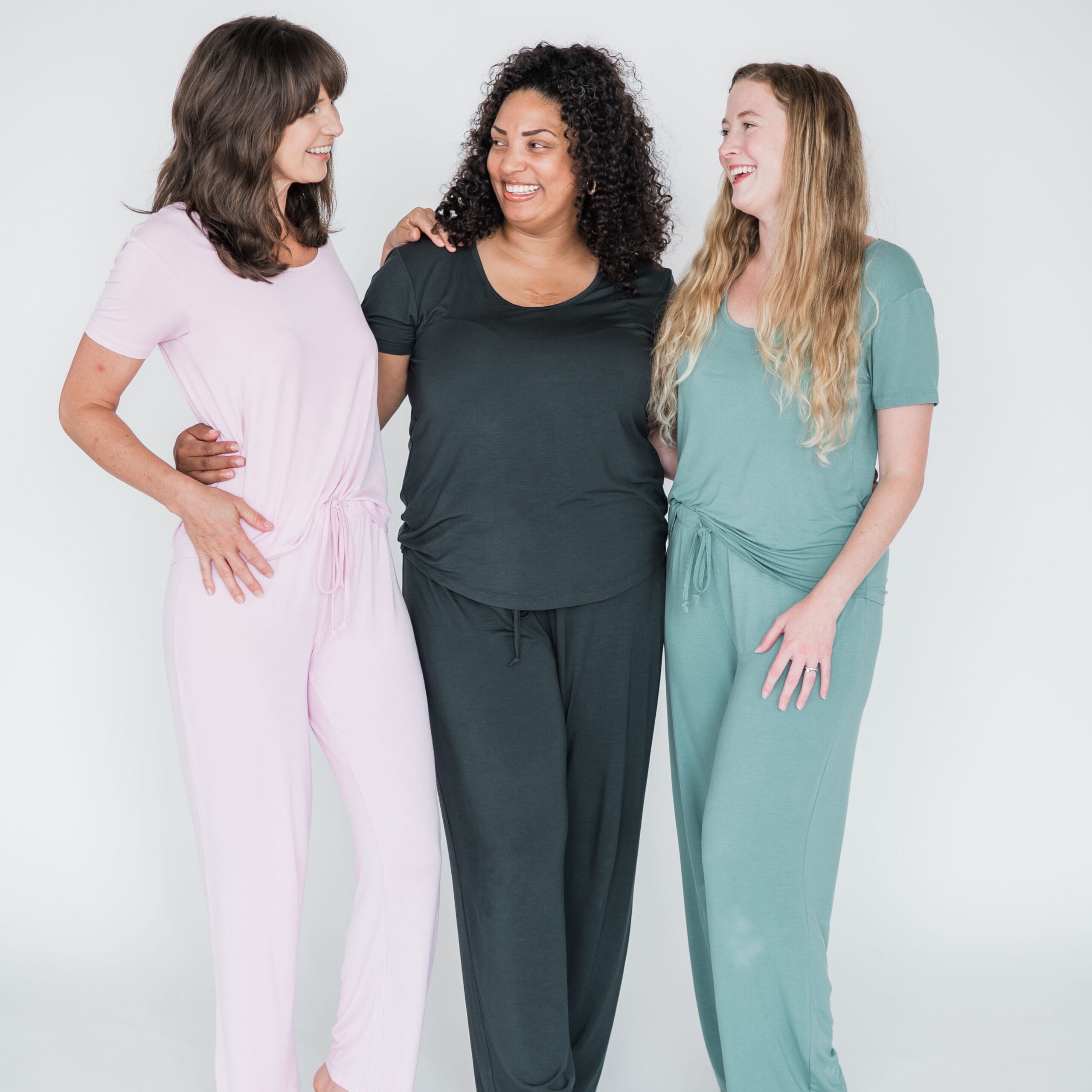 Three women wearing soft, loose-fitting pajama sets in neutral and pastel tones against a clean studio background.