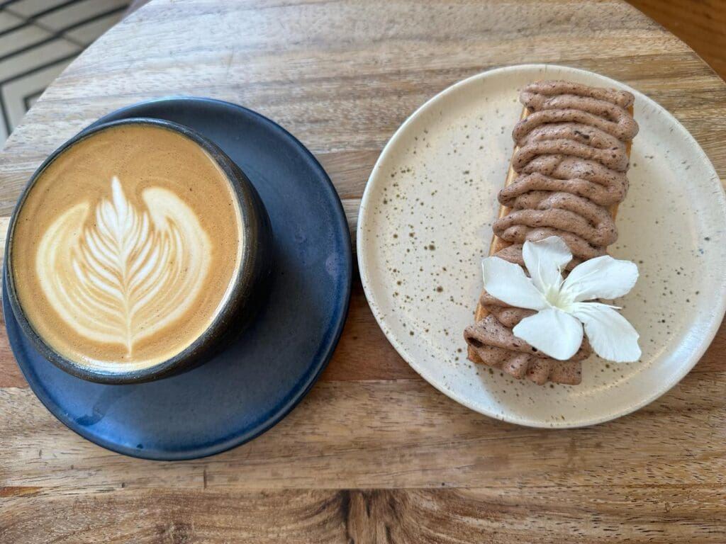 A latte with leaf latte art and pastry topped with cream and flower on plate at Casa Cafetzin cafe in El Paso Texas.