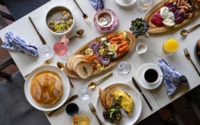 A spread of brunch foods: pancakes eggs, coffee, charcuterie boards on a talbe at Greenfinch, Estancia La Jolla Hotel & Spa.