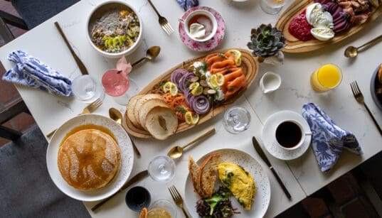 A spread of brunch foods: pancakes eggs, coffee, charcuterie boards on a talbe at Greenfinch, Estancia La Jolla Hotel & Spa.