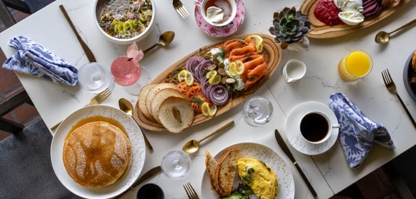 A spread of brunch foods: pancakes eggs, coffee, charcuterie boards on a talbe at Greenfinch, Estancia La Jolla Hotel & Spa.