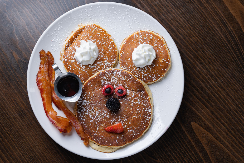 Pancakes styled with mouse ears, with fruit and powdered sugar alongside bacon and syrup at eggstasy in Phoenix.