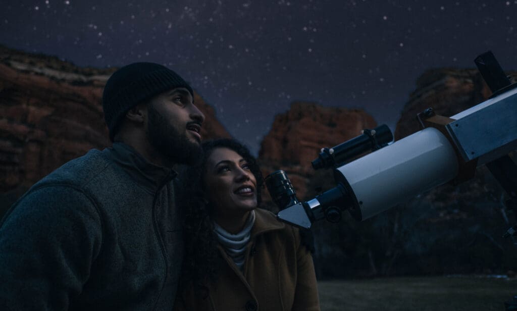 Couple using telescope under starry sky at Enchantment Resort Sedona during Dark Sky Week stargazing experience.