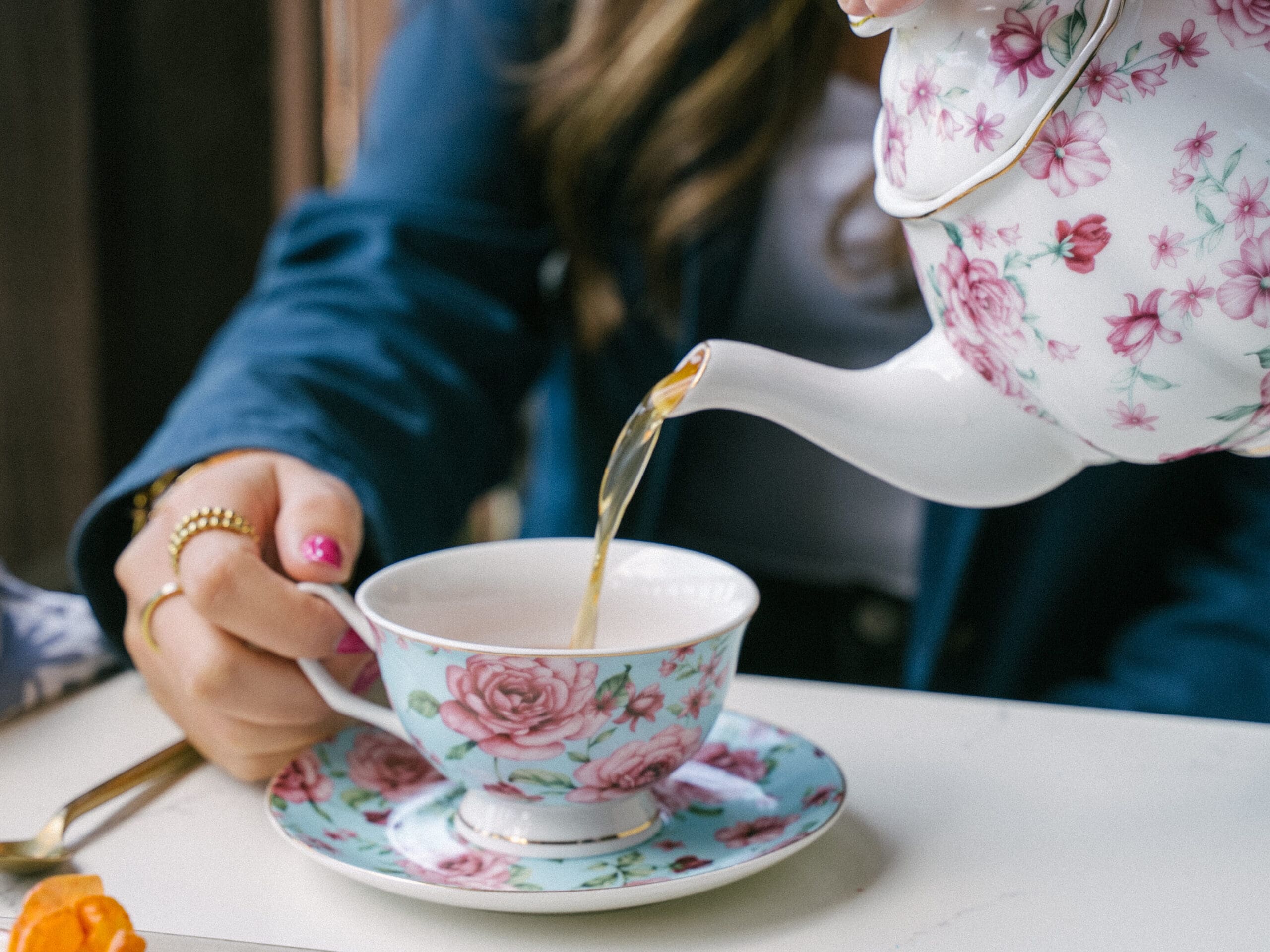 A person pours tea from an ornate tea pot into a matching tea cup that a guests holds at Greenfinch Restaurant in La Jolla.