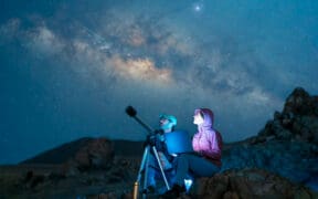 Couple sitting in the desert watching the stars and Milky Way next to a telescope in Utah.