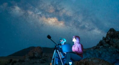 Couple sitting in the desert watching the stars and Milky Way next to a telescope in Utah.