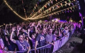 Large crowd gathered at an outdoor concert at night with string lights and colorful flags overhead at Flagstaff Hullabaloo Festival.