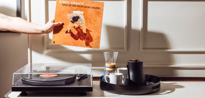 Hand holding Robert Johnson vinyl record near record player in hotel room with coffee setup at Gunter Hotel San Antonio.