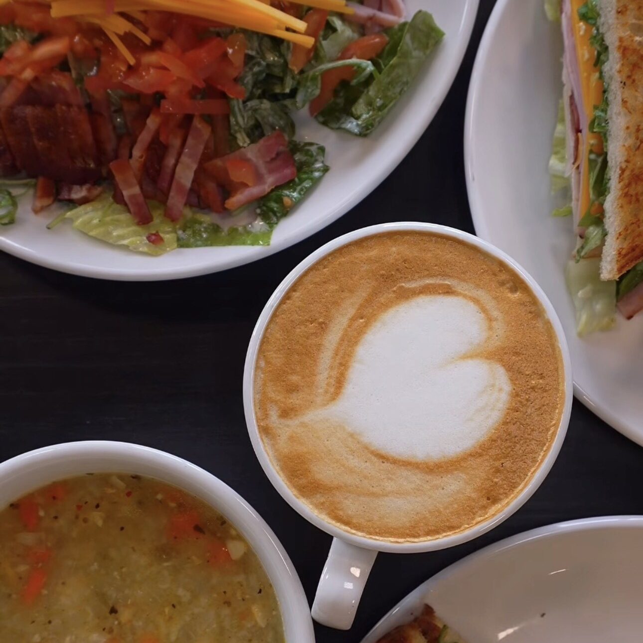 Latte with heart foam art surrounded by a sandwich, soup and salad on a table at Hayden House Café.
