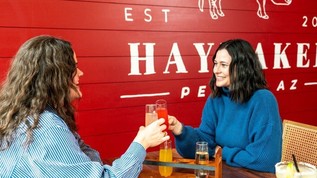 Two people toasting with mimosas at Haymaker restaurant in Arizona.