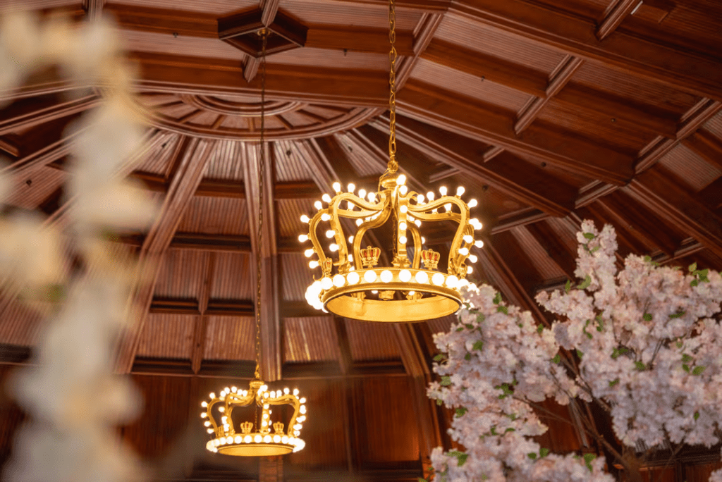 Two lit crown chandeliers hanging from the ceiling of the Hotel Del Coronado surrounded by cherry blossom trees.