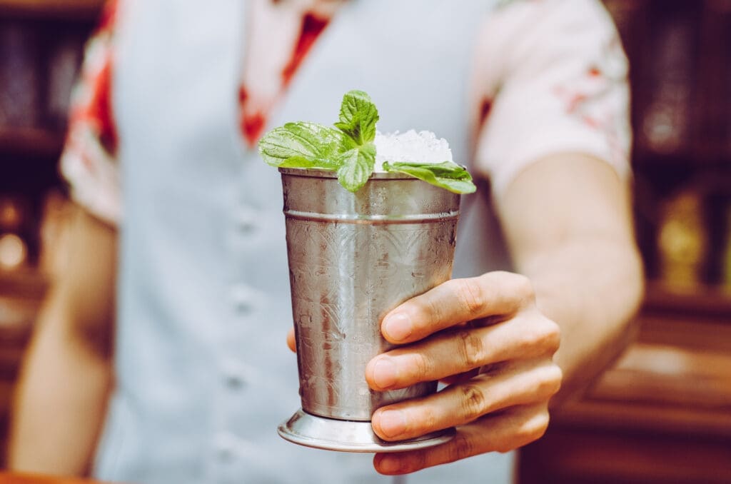 Close-up of a mint julep cocktail in a metal cup with fresh mint garnish, representing a classic Kentucky Derby drink at a rooftop bar setting.