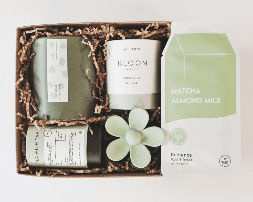 A curated self-care gift box with tea, bath products, a skincare mask and wellness items arranged in a cardboard box with filler.