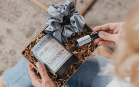 A curated self-care gift box with herbal tea, a satin scrunchie and an essential oil roller, styled in a cozy setting.
