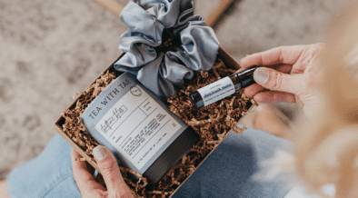 A curated self-care gift box with herbal tea, a satin scrunchie and an essential oil roller, styled in a cozy setting.
