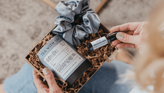 A curated self-care gift box with herbal tea, a satin scrunchie and an essential oil roller, styled in a cozy setting.