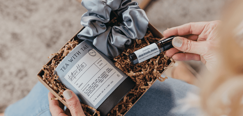 A curated self-care gift box with herbal tea, a satin scrunchie and an essential oil roller, styled in a cozy setting.
