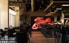 Chef preparing sushi at Odd Rabbit in Boulder with neon fish artwork and modern bar seating.