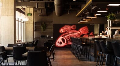 Chef preparing sushi at Odd Rabbit in Boulder with neon fish artwork and modern bar seating.