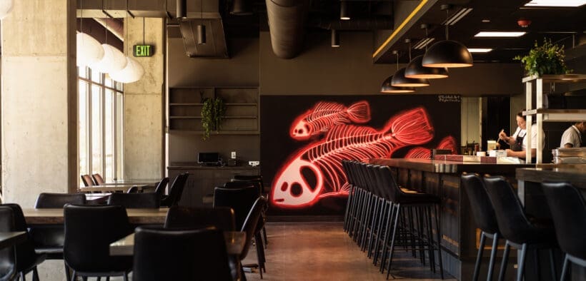 Chef preparing sushi at Odd Rabbit in Boulder with neon fish artwork and modern bar seating.