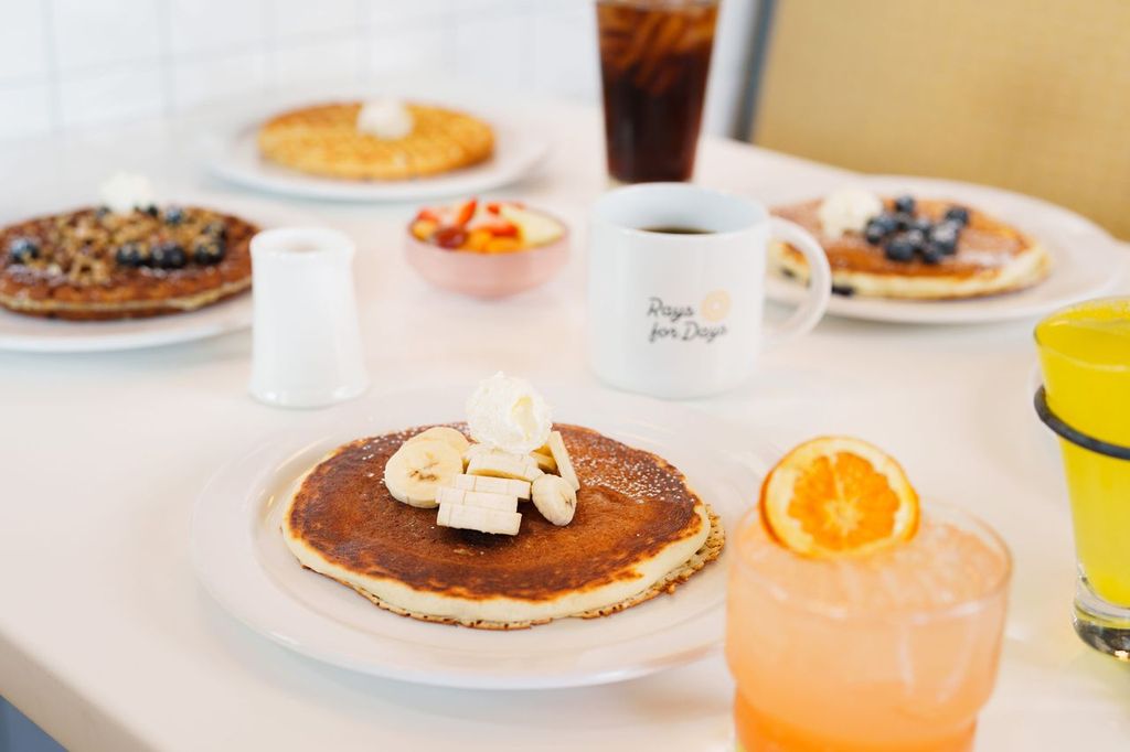 Pancakes topped with banana slices served with drinks and breakfast dishes at Over Easy.