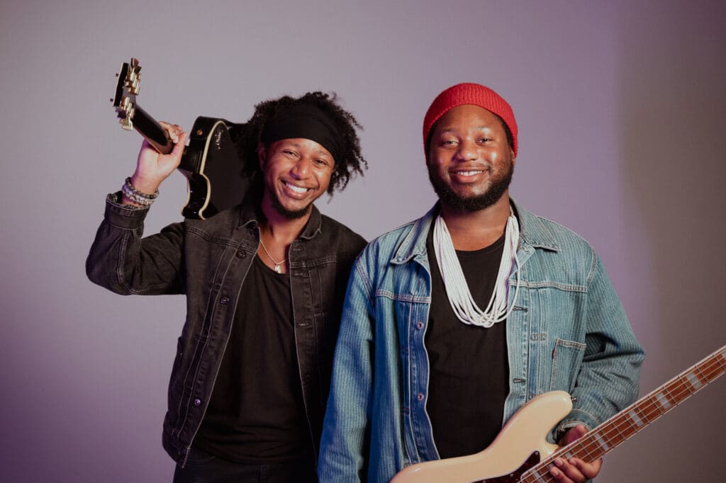 The Peterson Brothers musicians holding guitar and bass posing together ahead of San Antonio blues performance.