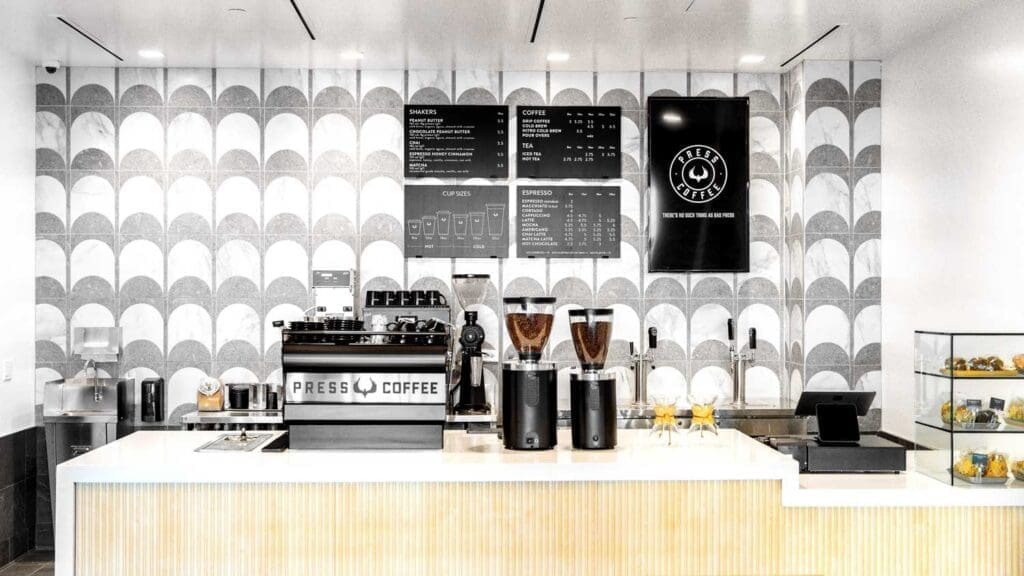 Modern coffee bar with espresso machines, menu boards and minimalist tiled design at Press Coffee.