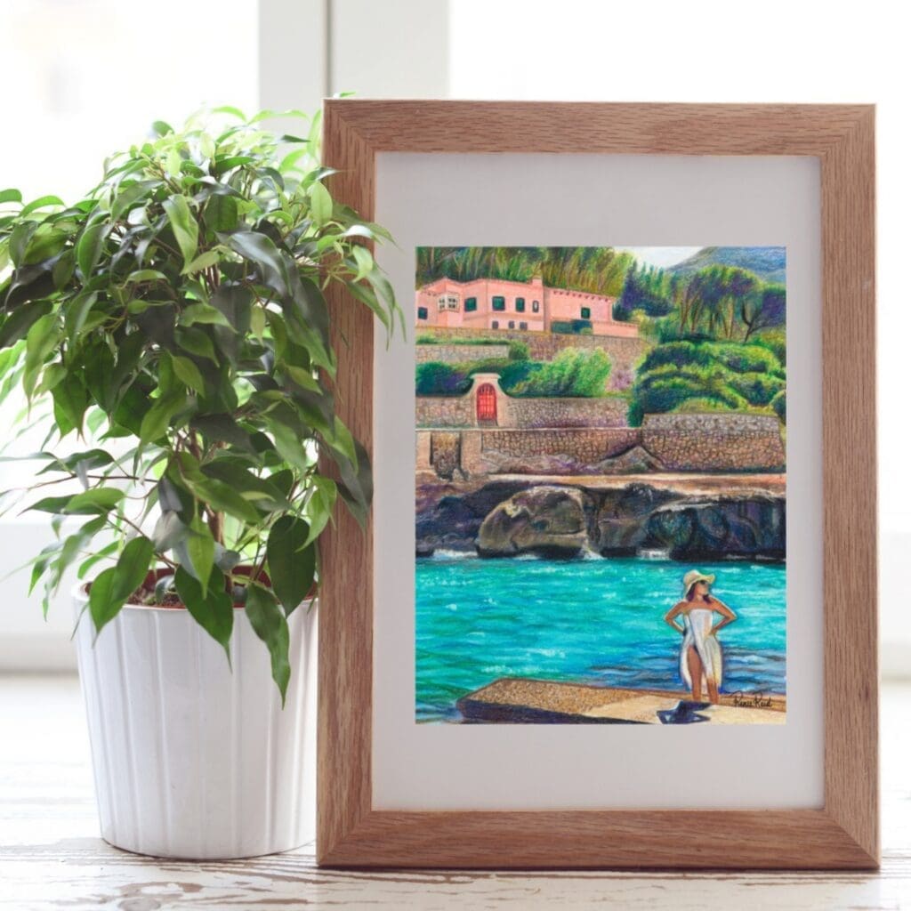 A framed coastal art print displayed next to a green houseplant on a bright windowsill.