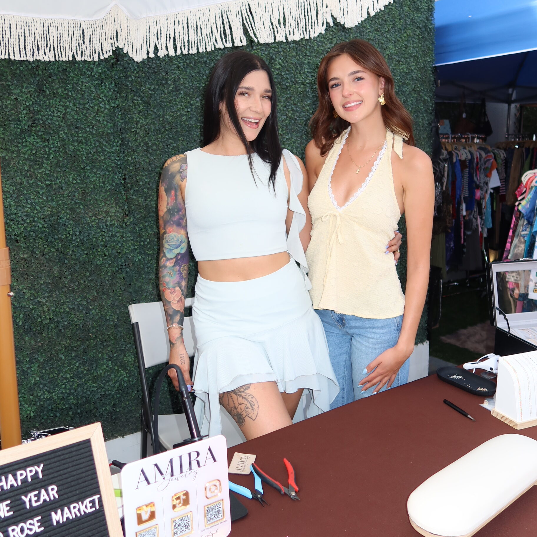 Two women at Amira Jewelry vendor booth at Rodeo Rose Market showcasing handmade jewelry and interacting with customers.
