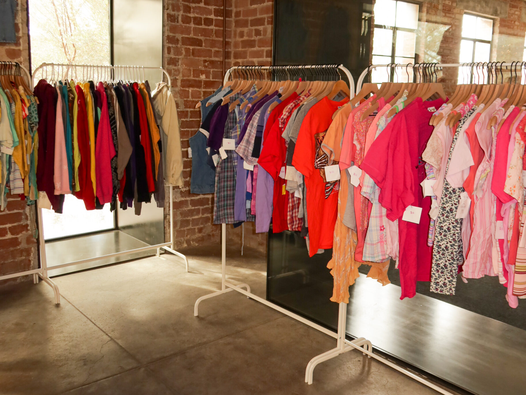 Racks of colorful vintage clothing inside Rodeo Rose Market vendor space with brick walls and modern interior.
