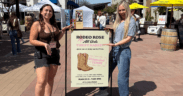 Trinity Roraback and Erin Thorburn standing at Rodeo Rose Market in Tempe Arizona with event sign and vendor tents in background.